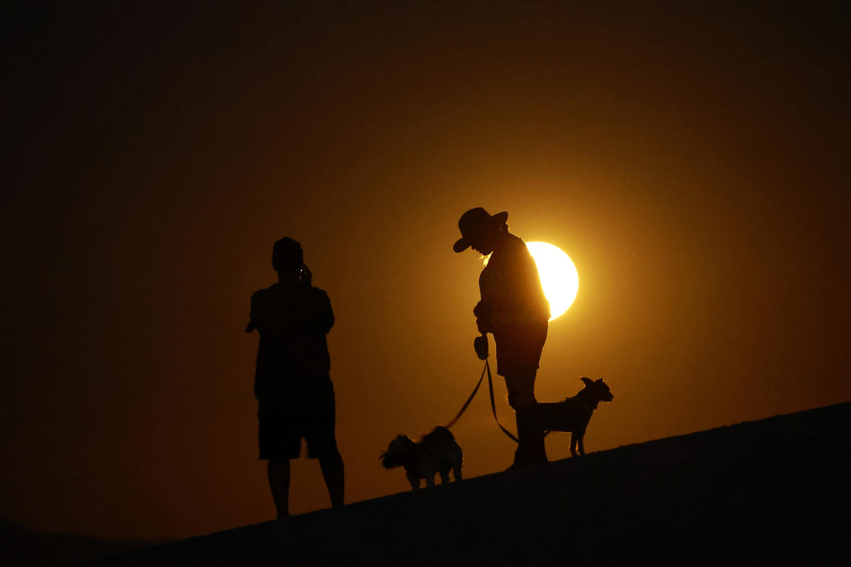 The outlines of two people with two small animals as the supermoon rises.