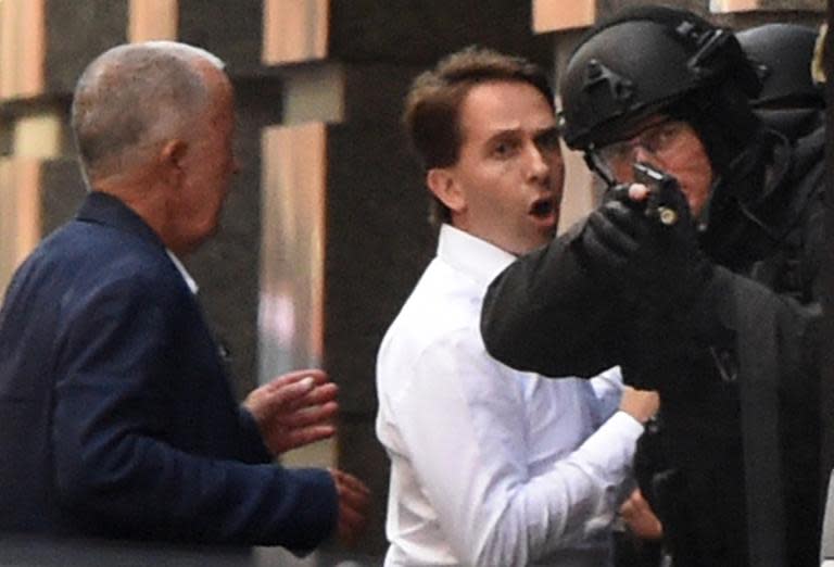 Two hostages (L) run for cover behind a policeman (R) during a hostage siege in the central business district of Sydney on December 15, 2014