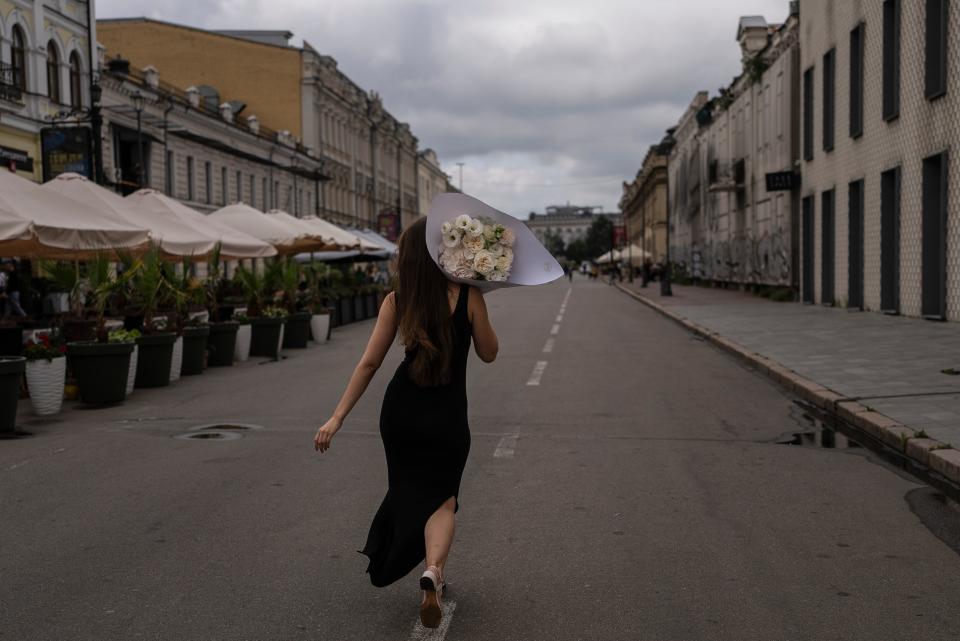 A woman walks with a bouquet of flowers during a photoshoot in the Podil neighborhood of Kyiv (AP)