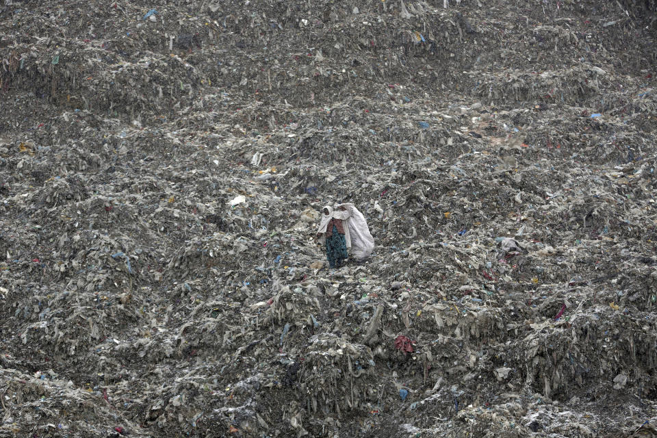 In this Tuesday, Dec. 11, 2018 photo a woman who scavenges recyclable materials from garbage for a living walks across a mountain of garbage at the dump on the outskirts of Kabul, Afghanistan. (AP Photo/Massoud Hossaini, File)