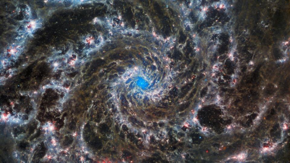 The Phantom Galaxy as imaged by the James Webb Space Telescope is a spiral of browns and pinks with starfields visible in the gaps and a turquoise center