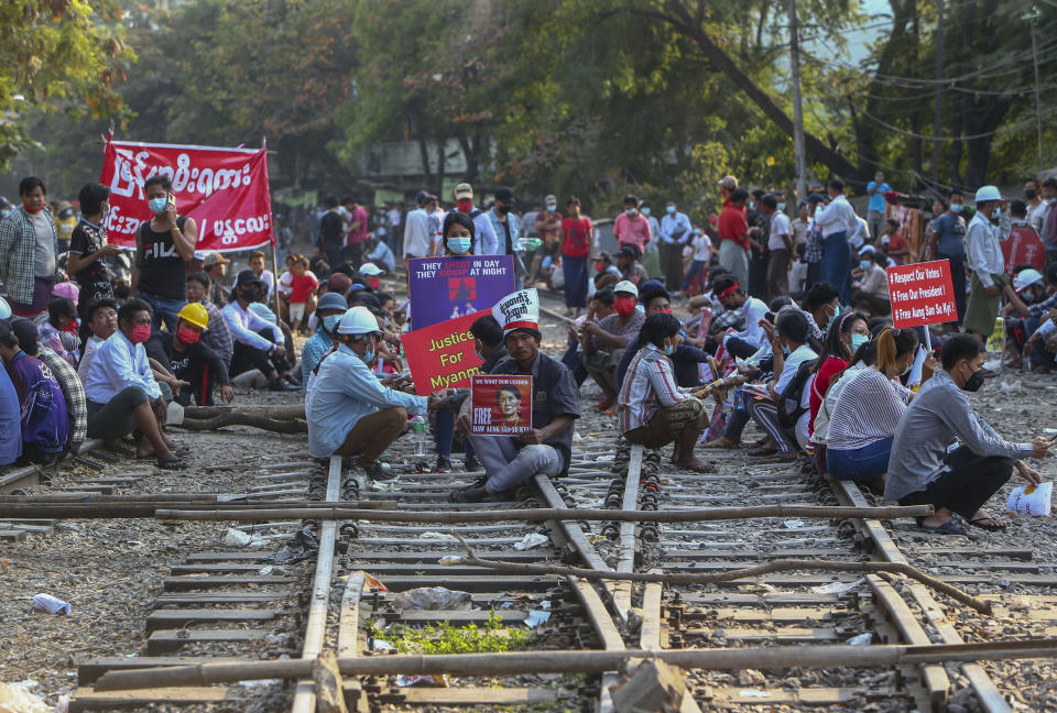 FILE - In this Feb. 17, 2021, file photo, demonstrators with placards sit on the railway tracks in an attempt to disrupt train service during a protest against the military coup in Mandalay, Myanmar. Political turmoil and disruptions following the coup in Myanmar could undo years of progress and double the number of its people living in poverty to nearly half the population, a United Nations report said Friday, April 30, 2021. (AP Photo/File)