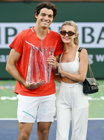 <p>John Cordes/Icon Sportswire via Getty</p> Taylor Fritz of the United States holds the championship trophy with girlfriend Morgan Riddle after winning a finals tennis match