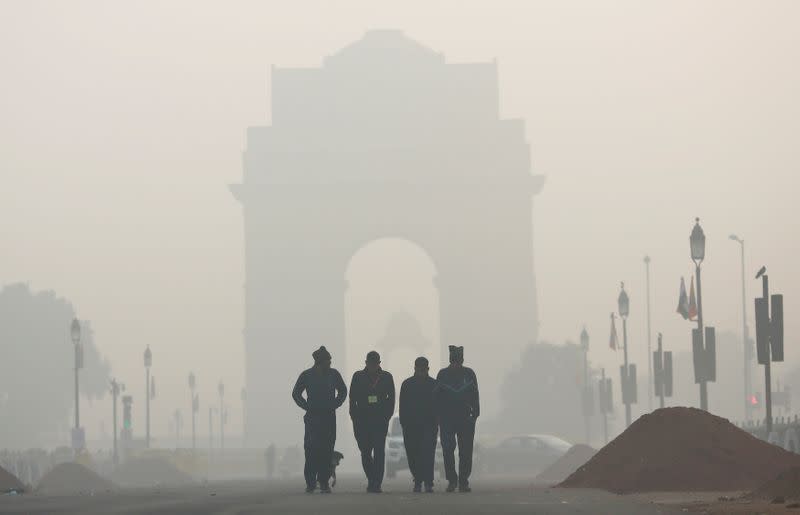 FILE PHOTO: Men walk in front of the India Gate shrouded in smog in New Delhi