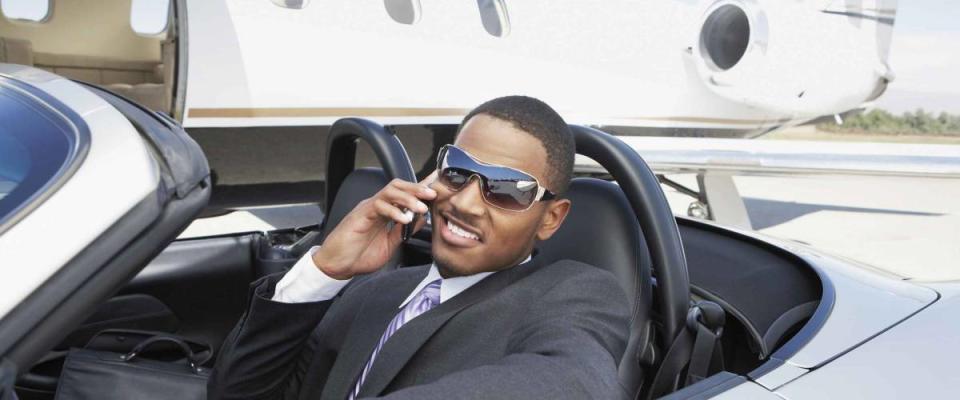 Young businessman using cell phone in convertible near private jet