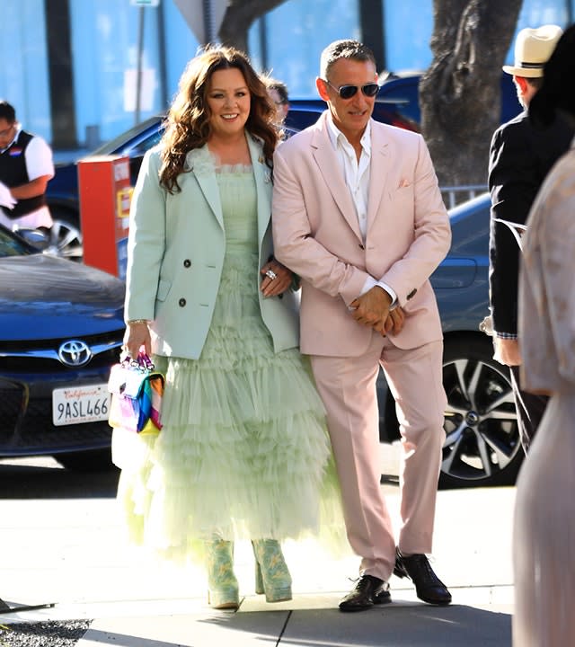 Melissa McCarthy in a mint green tulle dress with a matching blazer walks with director Adam Shankman in a light pink suit