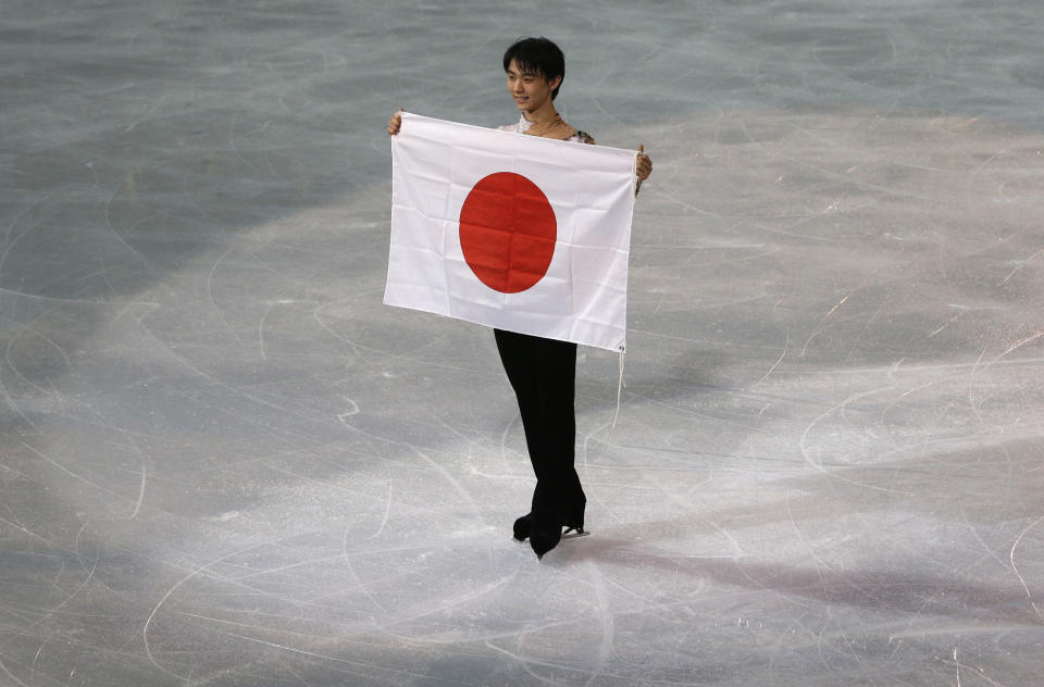 Yuzuru Hanyu of Japan poses with the national flag after he placed first in the men's free skate figure skating final following the flower ceremony at the Iceberg Skating Palace during the 2014 Winter Olympics, Friday, Feb. 14, 2014, in Sochi, Russia. (AP Photo/Darron Cummings)