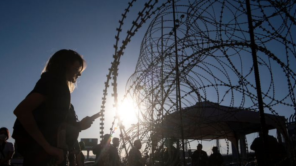 A young Ukrainian woman stands by a fence in the Mexico-US border