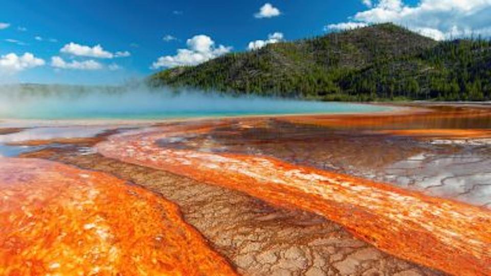 Close of of the Grand Prismatic Spring at Yellowstone, with steam rising from the water and a mountain in the background