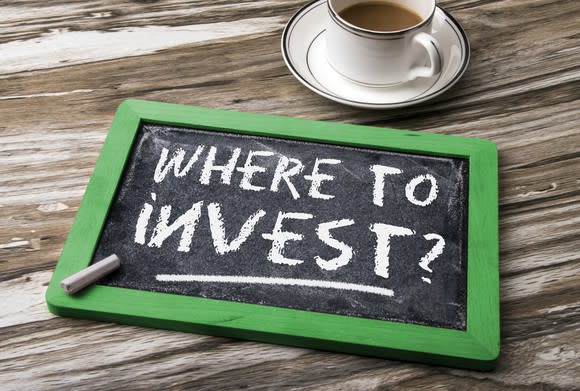 Chalk slate on a table next to a coffee cup with "where to invest?" written on it.