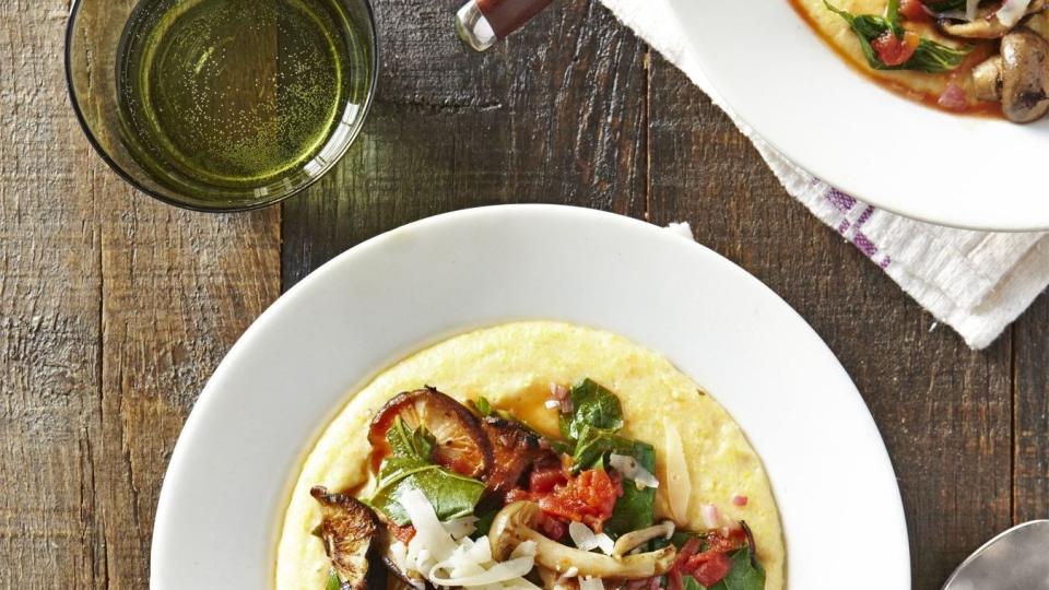 creamy polenta with mushrooms and collards in a white bowl with a spoon