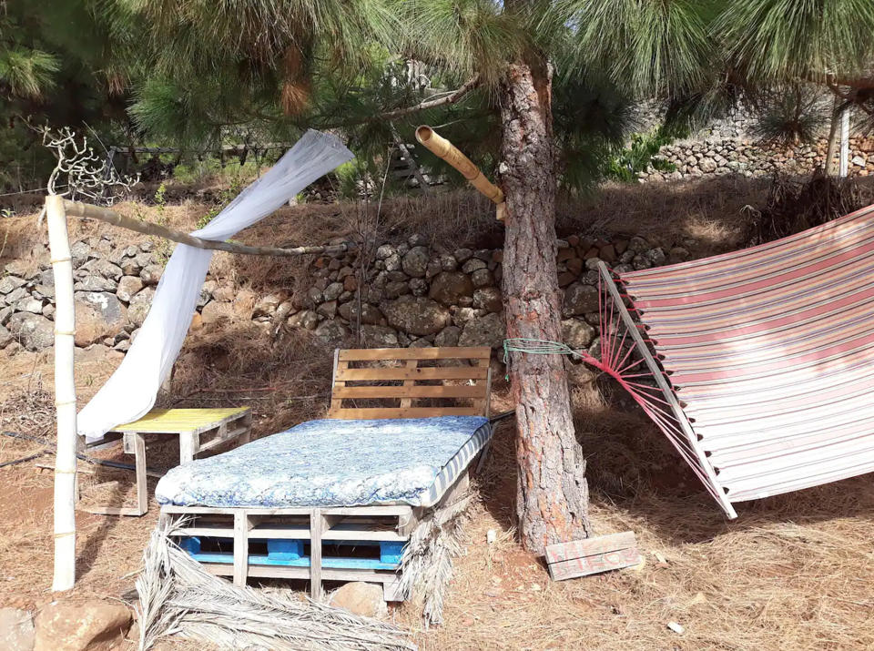 The pallet bed under a tree and next to a hammock. 