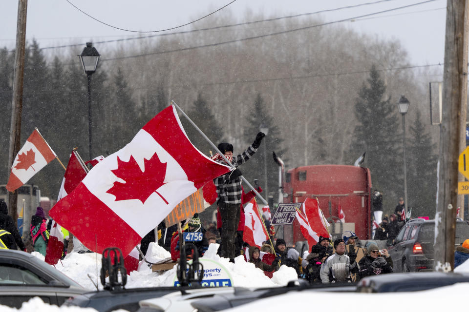 Protesters and supporters against a COVID-19 vaccine mandate for cross-border truckers cheer as a parade of trucks and vehicles pass through Kakabeka Falls outside of Thunder Bay, Ontario, on Wednesday, Jan. 26, 2022. (David Jackson/The Canadian Press via AP)