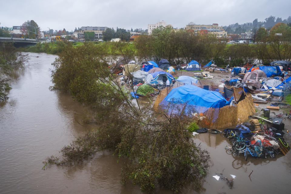 Bloated by heavy rains, the San Lorenzo River partially floods a homeless encampment at Riverwalk Park in Santa Cruz, Calif., Monday, Dec. 13, 2021. A major storm hitting Northern California is expected to intensify and bring travel headaches and a threat of localized flooding after an abnormally warm fall in the U.S. West. (AP Photo/Nic Coury)