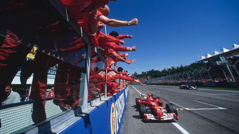 A photo of crowds cheering on a red Ferrari f1 car as it crosses the line. 