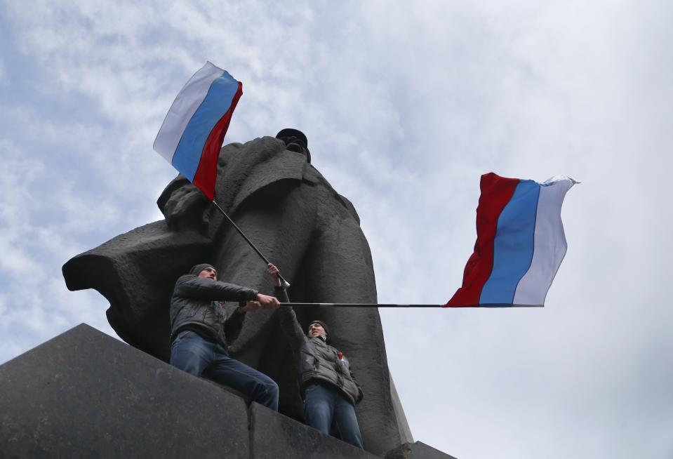 Men wave Russian national flags underneath a statue of Soviet revolutionary leader Vladimir Lenin during a pro Russian rally at a central square in Donetsk, eastern Ukraine, Sunday, March 9, 2014. Following an extraordinary meeting of the Ukrainian government, Prime Minister Arseniy Yatsenyuk announced he would be flying later this week to the United States for high-level talks on "resolution of the situation in Ukraine," the Interfax news agency reported Sunday. (AP Photo/Sergei Grits)