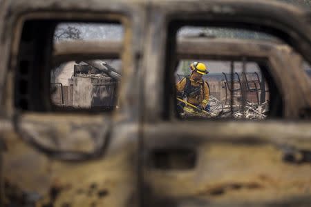 A firefighter is seen through destroyed cars as he searches for victims in the rubble of a home burnt by the Valley Fire in Middletown, California, September 14, 2015. REUTERS/David Ryder