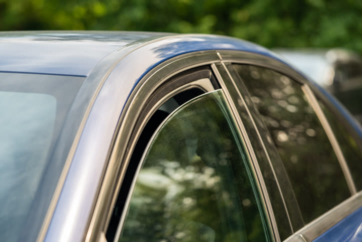 Close-up of a car's partially open window with a green, blurry, natural background visible through the window