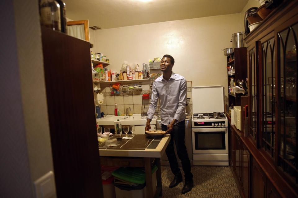 In this photo dated Thursday, Feb. 2, 2017, Cheikh Ahmed, a refugee from Guinea poses while standing in the kitchen of the house belonging to his hosts, Murielle and Loic Gandais, in Palaiseau, south of Paris France. When the Gandais family decided to host a refugee at their home in a middle class neighborhood outside Paris, they assumed their guest would be a Syrian or an Iraqi fleeing war. Instead, a 25-year-old journalist with a young family in the former French colony of Guinea is the person sleeping gratefully in a spare bedroom, sharing unfamiliar food and nourishing hopes for a better life. (AP Photo/Christophe Ena)