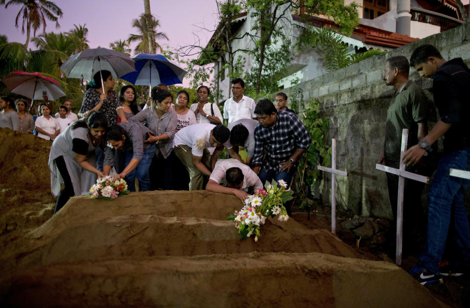 FILE - In this Monday, April 22, 2019 file photo, relatives place flowers after the burial of three from the same family, all victims of Easter Sunday's bomb blast at St. Sebastian Church, in Negombo, Sri Lanka. Roughly 250 people died in six coordinated suicide bombings that ripped through Sri Lanka on Easter Sunday. (AP Photo/Gemunu Amarasinghe, File)