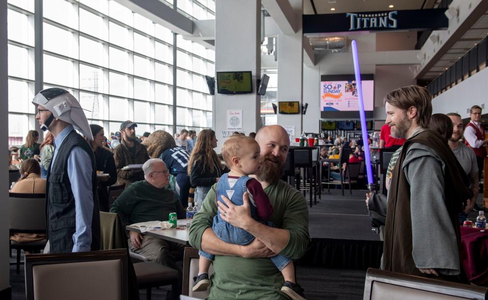 Members of the rebel Legion, Gunner Goodlad, as a Rebel Fleet Trooper, and Jeff Key, as Obi Wan Kenobi, walk by as Craig Cato holds Duncan Cato, 1, during a lunch event for children from Our Kids, a nonprofit serving children and families affected by child sexual abuse at Nissan Stadium in Nashville , Tenn., Sunday, Feb. 19, 2023.