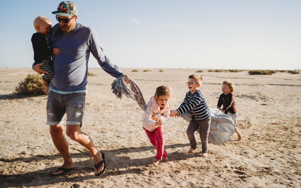 Father and happy children playing with towel at beach on chilly day