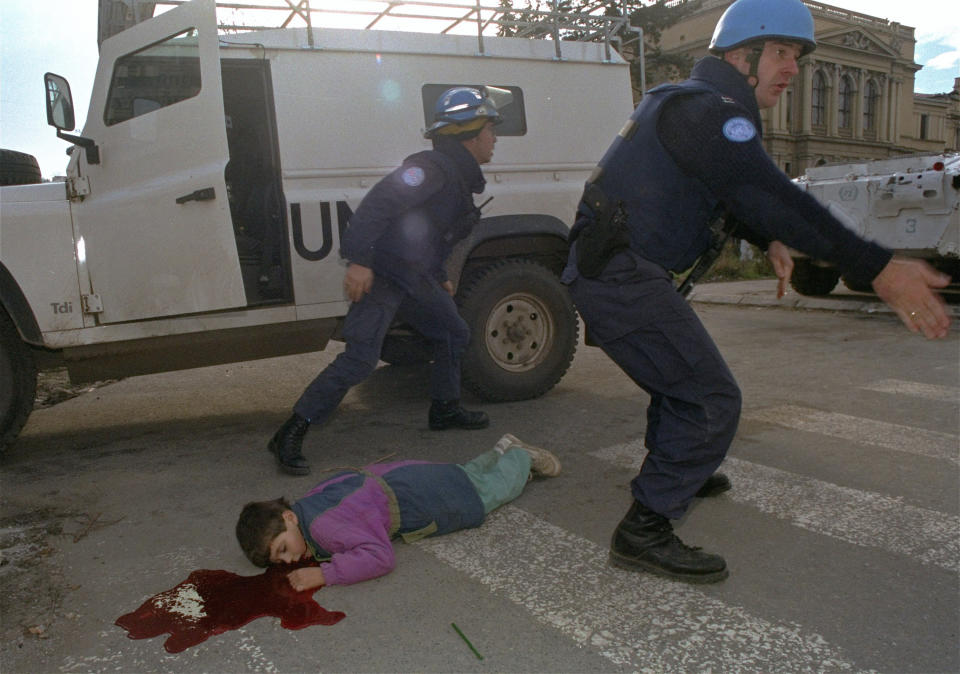 FILE - Seven-year-old Nermin Divovic lies mortally wounded in a pool of blood after he was shot in the head as U.S. and British U.N. firefighters arrive to assist in Sarajevo, Nov. 18, 1994. The boy was killed by a sniper firing from an apartment building along the notorious Sniper Alley in the city's center. The firefighters were at his side almost immediately, but the boy died. (AP Photo/Enric Marti, File)