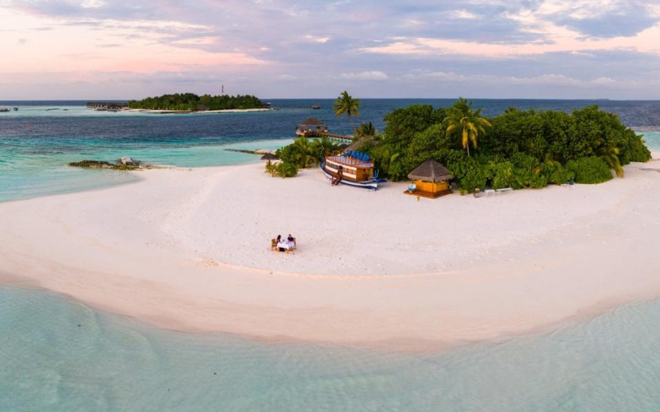 Aerial drone footage of adult couple having dinner on the sandy beach of a private island