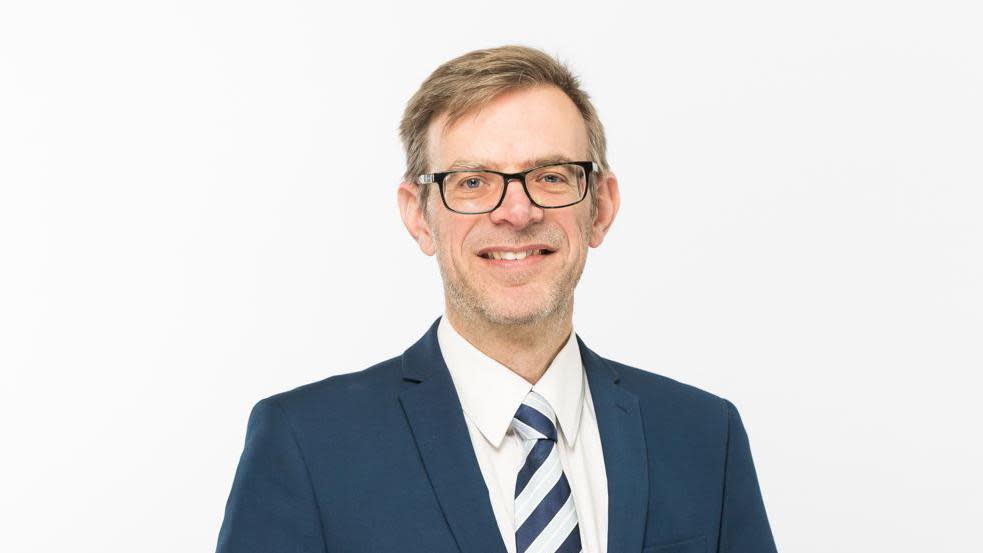 Mark Westwood in a jacket, shirt and tie smiling at the camera