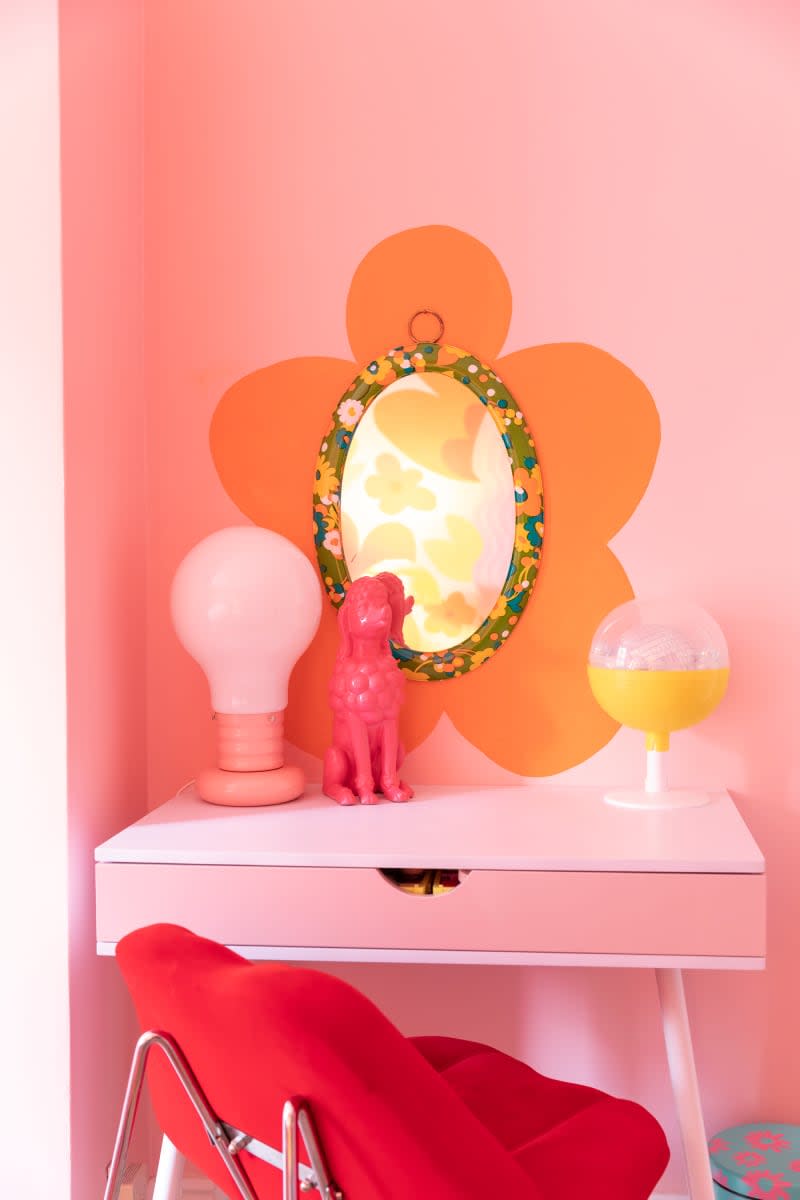 Small vanity with vintage mirror in front of orange floral motif.