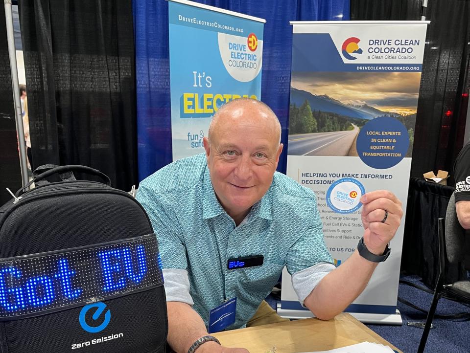 Nigel Zeid smiling while holding up a badge and standing at a table at an industry event.