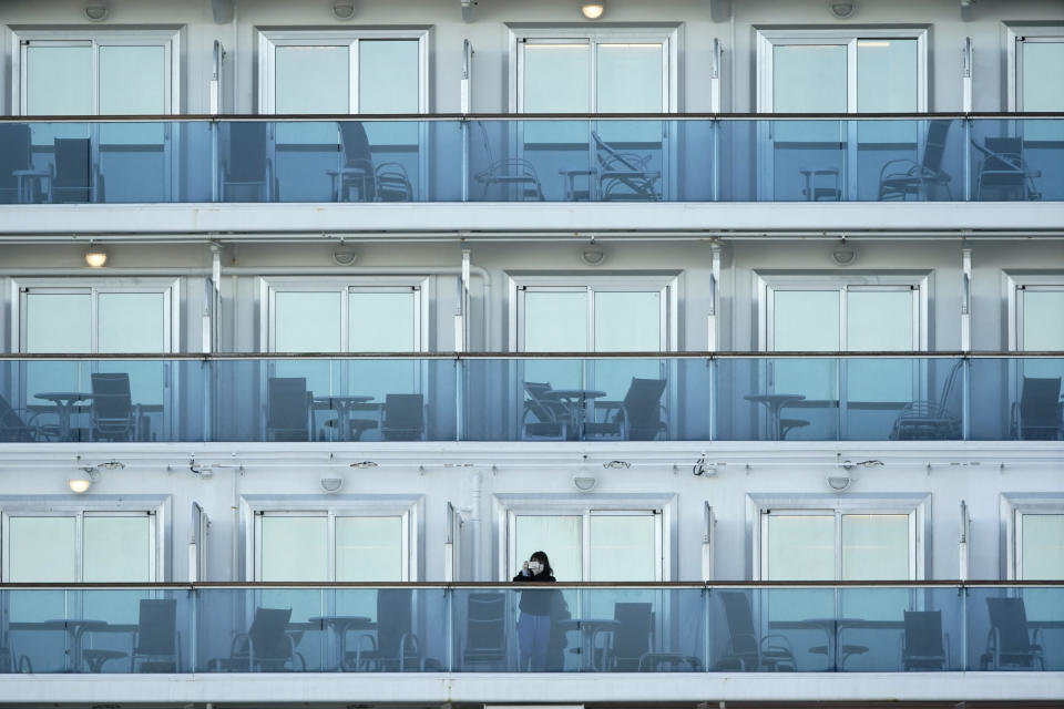 A passenger stands on the balcony of the cruise ship Diamond Princess anchored at the Yokohama Port, near Tokyo Thursday, Feb. 6, 2020. Health workers said 10 more people from the Diamond Princess were confirmed ill with the virus, in addition to 10 others who tested positive on Wednesday. They were dropped off as the ship docked and transferred to nearby hospitals for further test and treatment. (AP Photo/Eugene Hoshiko)