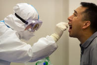 A worker in a protective suit takes a throat swab for a COVID-19 test in Wenchang in southern China's Hainan Province, Sunday, Nov. 22, 2020. Authorities are conducting mass testing and shutting down schools after China reported three new domestically transmitted cases in the past 24 hours - two in northern Inner Mongolia province and one in Shanghai. (AP Photo/Mark Schiefelbein)