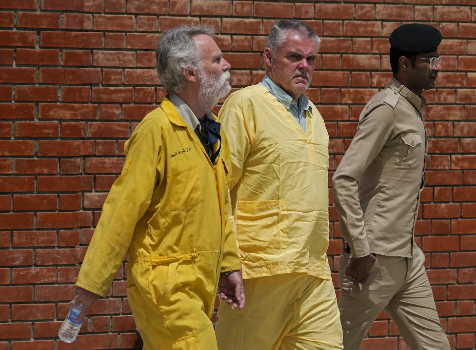 FILE - Jim Fitton of Britain, left, and Volker Waldman of Germany, center, wearing yellow detainees' uniforms and handcuffed, are escorted by Iraqi security forces, outside a courtroom, in Baghdad, Iraq, on May 22, 2022. Fitton was sentenced Monday, June 6, by an Iraqi court to 15 years in prison on charges of smuggling artifacts out of the country, in a case that has attracted international attention. Waldman, tried with Fitton, was found not to have criminal intent in the case and will be released. (AP Photo/Hadi Mizban, File)