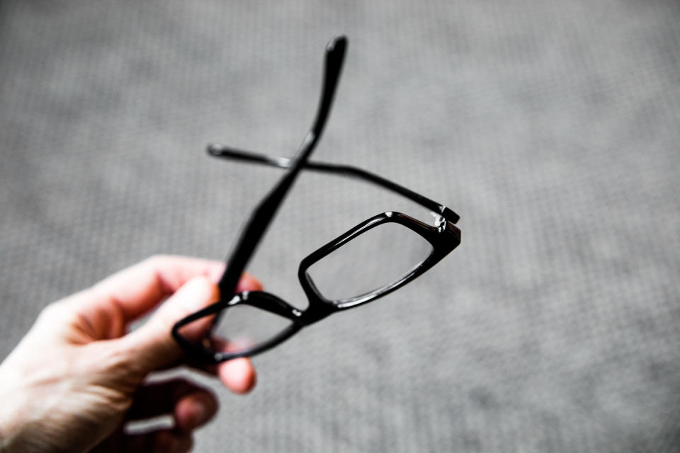 A hand holding a pair of black rimmed glasses