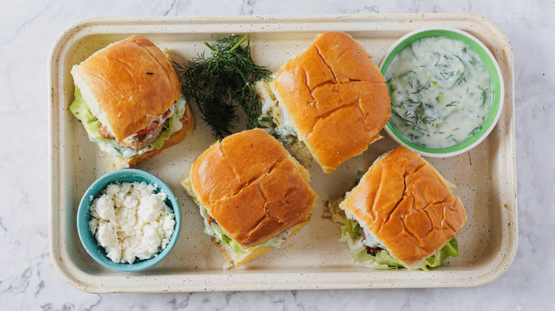 A baking sheet with four sliders, feta and tzatziki sauce