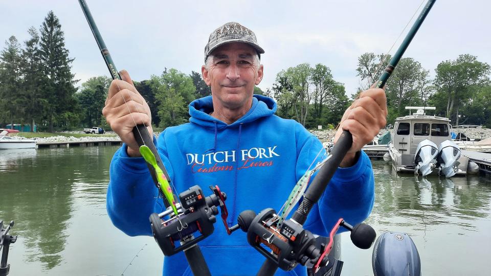 Capt. Keith Eshbaugh holds two of his fishing rods that have the colorful minnow imitation lures that have been successful for catching walleyes on Lake Erie. He paints his own lures.