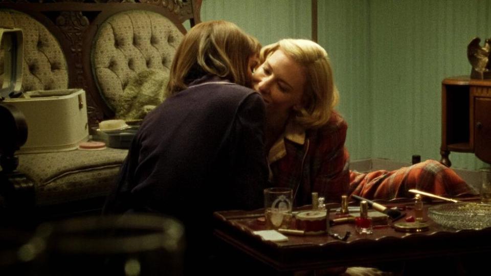 Two women gently kiss and nuzzle while sitting on the floor