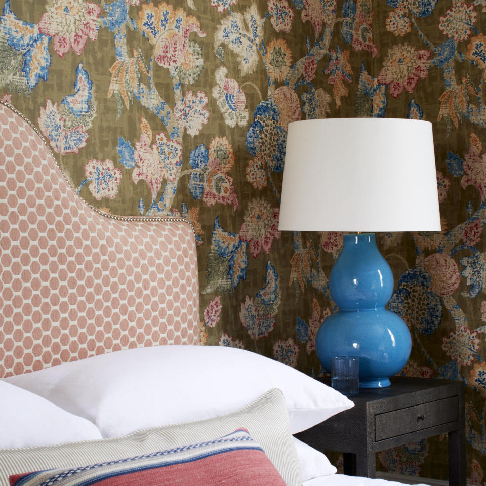 bedroom with fabric style wallpaper on walls, blue table lamp, upholstered headboard pink, white bedding