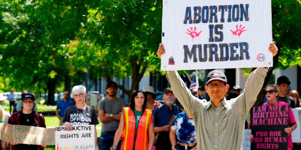 A man supporting restrictions on abortion holds a sign as abortion-rights supporters hold signs behind him outside the South Carolina Statehouse on Thursday, July 7, 2022, in Columbia, S.C.