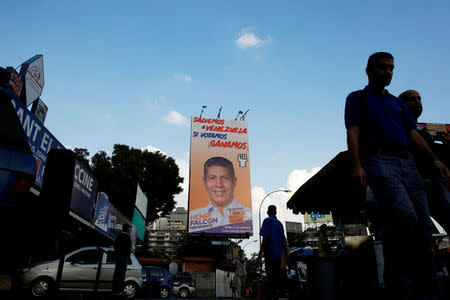 FILE PHOTO: People walk pass a campaign poster of Henri Falcon for the 2018 presidential elections in Caracas, Venezuela May 11, 2018. REUTERS/Carlos Jasso/File Photo