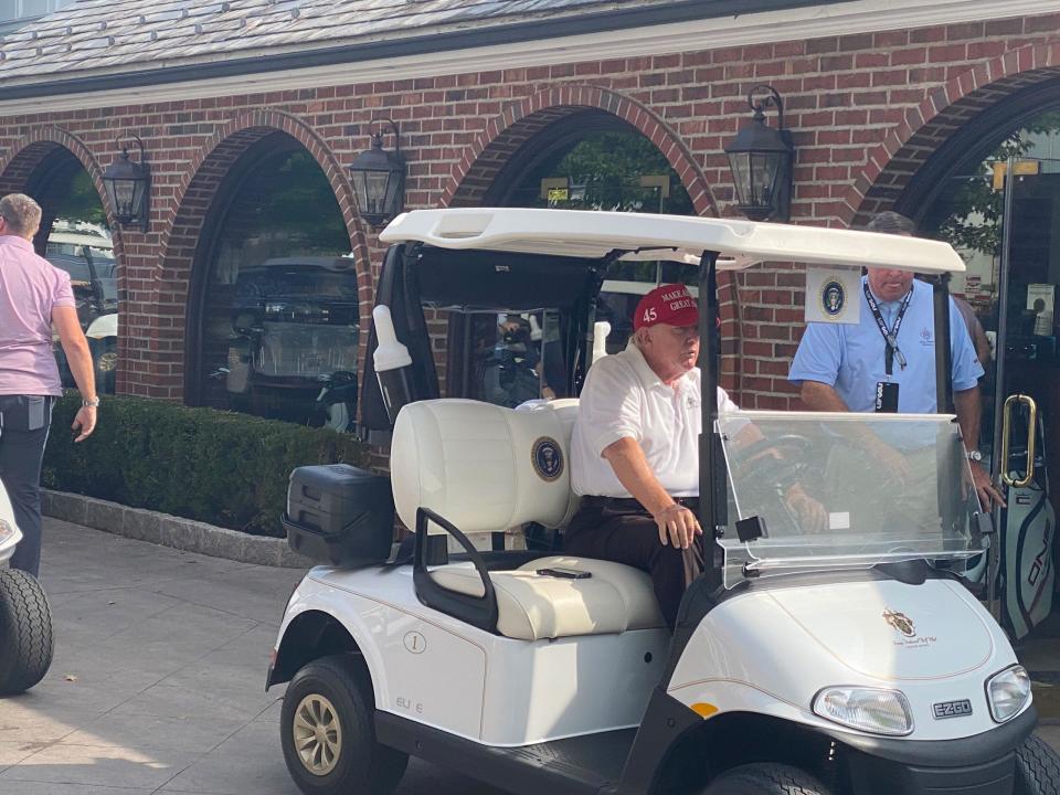 Donald Trump sits in his golf cart, which has the presidential seal on it.