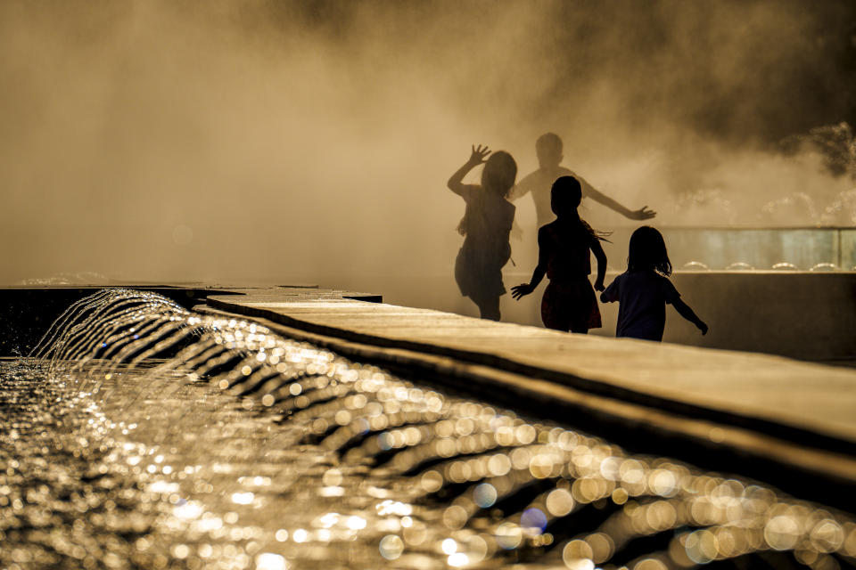 Children enjoy the drizzle from a public fountain before sunset in Bucharest, Romania, Thursday, June 20, 2024 as temperatures exceeded 38 degrees Celsius (100.4 Fahrenheit). The national weather forecaster issued a orange warning for western and southern Romania where temperatures are expected to reach 38 degrees Celsius (100.4 Fahrenheit) in the coming days. (AP Photo/Vadim Ghirda)