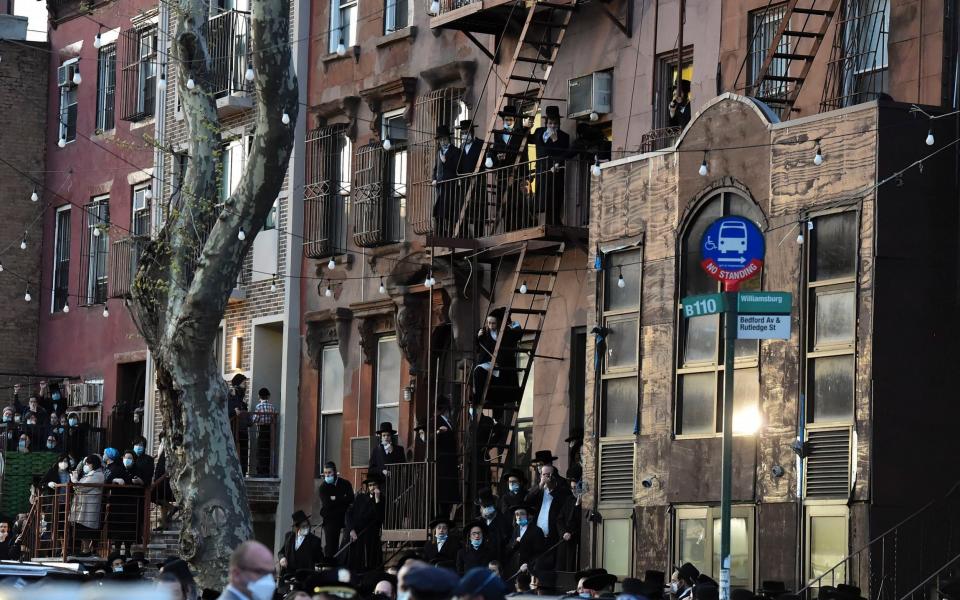 Residents of the Williamsburg neighborhood of the Brooklyn borough of New York stand on fire escapes as hundreds of mourners gather to observe a funeral for Rabbi Chaim Mertz - AP