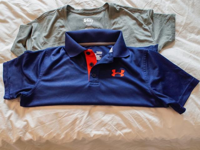 A folded navy blue polo with orange accents sits on top of a folded gray t shirt on a white sheet.