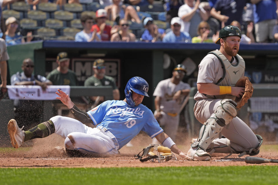 Kansas City Royals' Michael Massey (19) slides home to score on a three-run triple hit by Vinnie Pasquantino while Oakland Athletics catcher Kyle McCann waits for the throw during the sixth inning of a baseball game Sunday, May 19, 2024, in Kansas City, Mo. (AP Photo/Charlie Riedel)