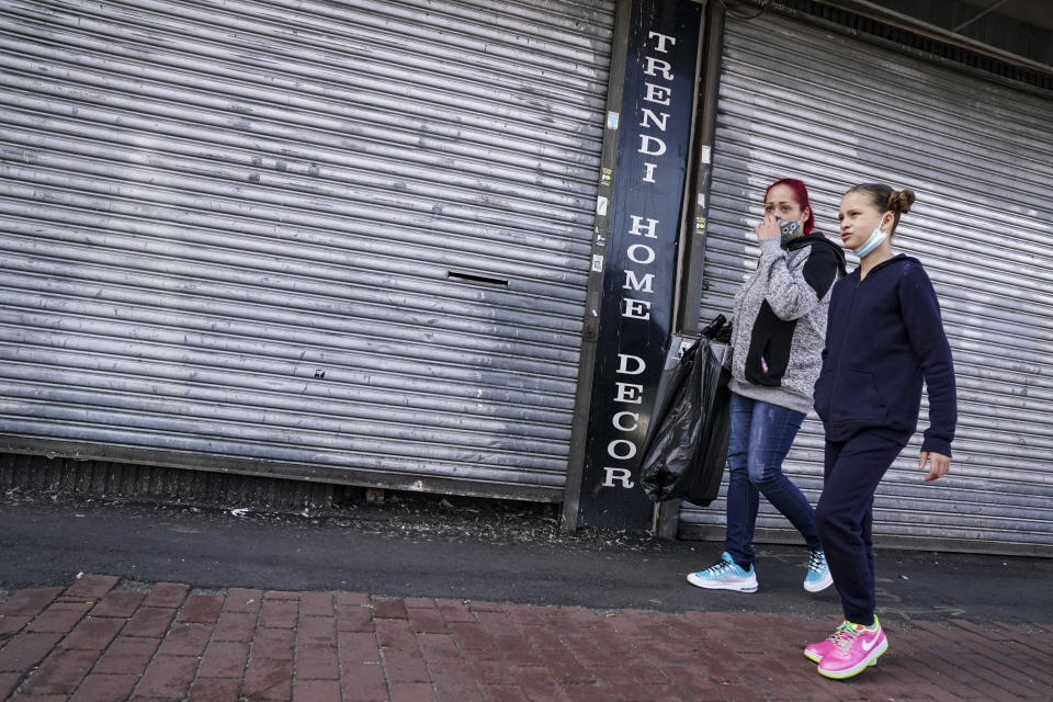 Pedestrians pass shuttered storefronts on Thursday, Oct. 15, 2020, as restrictions are imposed due to a COVID-19 infection increase in the Far Rockaway neighborhood of the borough of Queens in New York. After shutdowns swept entire nations during the first surge of the coronavirus earlier this year, some countries and U.S. states are trying more targeted measures as cases rise again around the world. (AP Photo/John Minchillo)