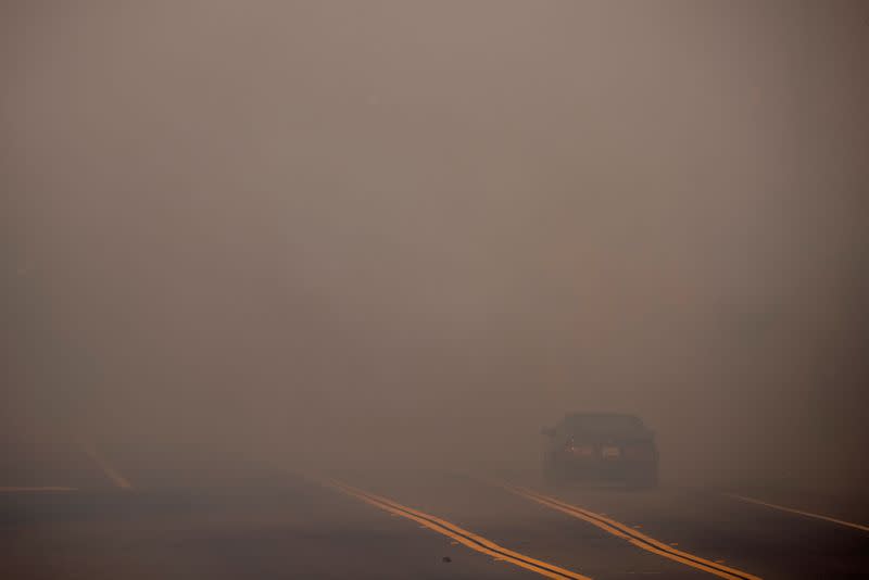 A motorist evacuating from the wind driven Bond Fire wildfire drives into a smoke filled highway near Lake Irvine in Orange County, California