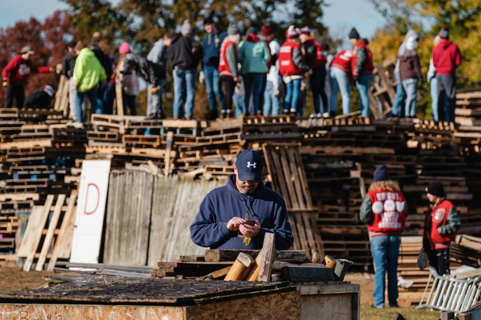 Dover High School calculus teacher Brian Miller consults his cellphone while students construct a stack of pallets and other pieces of wood Thursday for an evening bonfire at Crater Stadium. The bonfire is part of the annual Dover-Phila football rivalry week celebration.