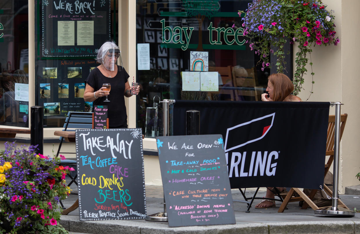 TENBY, WALES - JULY 16:  A woman at the Bay Tree delivers drinks to an outside sitting area on July 16, 2020 in Tenby, Wales. Welsh Pubs are allowed to open as long as they have outside drinking areas (Photo by Huw Fairclough/Getty Images)